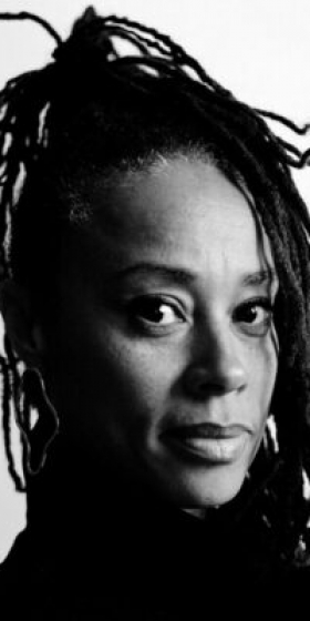 Black and white portrait of the black female artist jeanette ehlers with her long dread locs in a high ponytail looking at the camera at an angle and a high turtleneck sweater