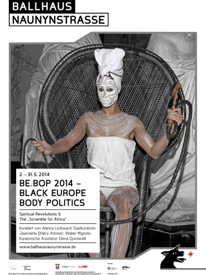 black woman covered in white paint sitting on a large black wicker chair and holding a long black whip in both hands